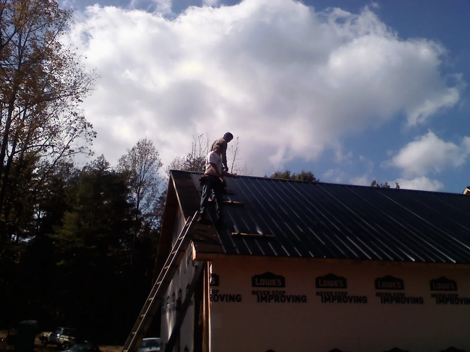 Roofer fastening dark metal panels high against a cloudy sky, from a Roof Inspection job in Emerson